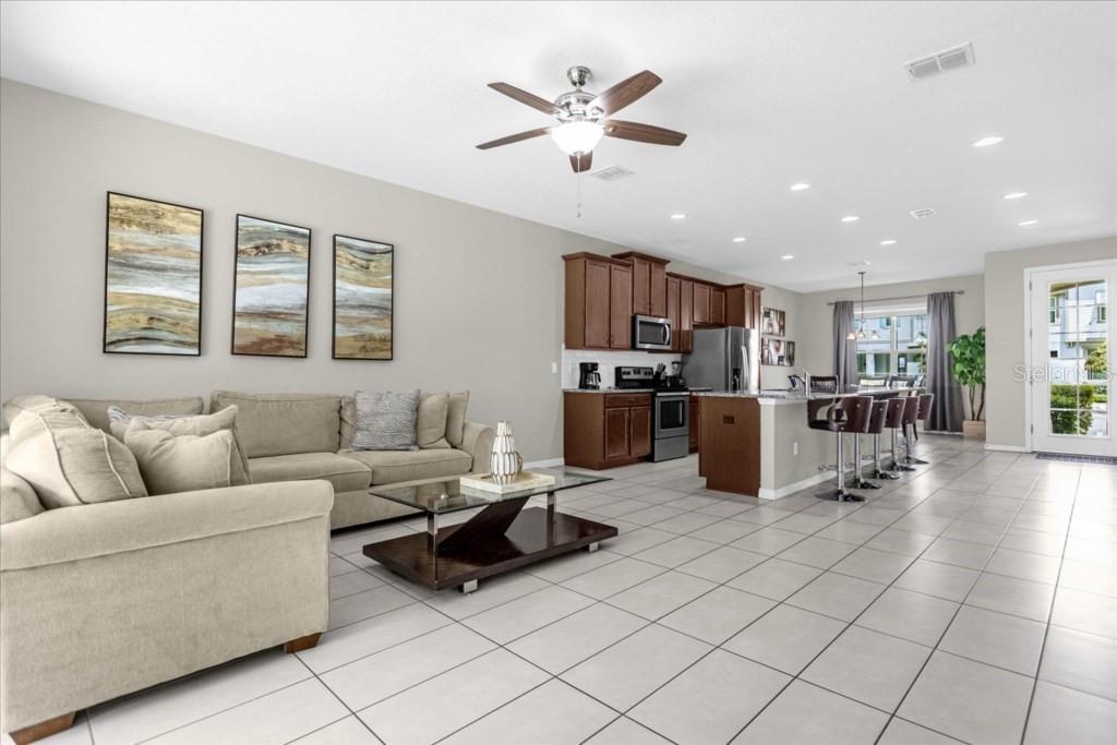 An open-concept living room and kitchen featuring tile flooring, dark wood cabinets, and neutral furniture — 1540 CAREY PALM CIRCLE, KISSIMMEE, FL