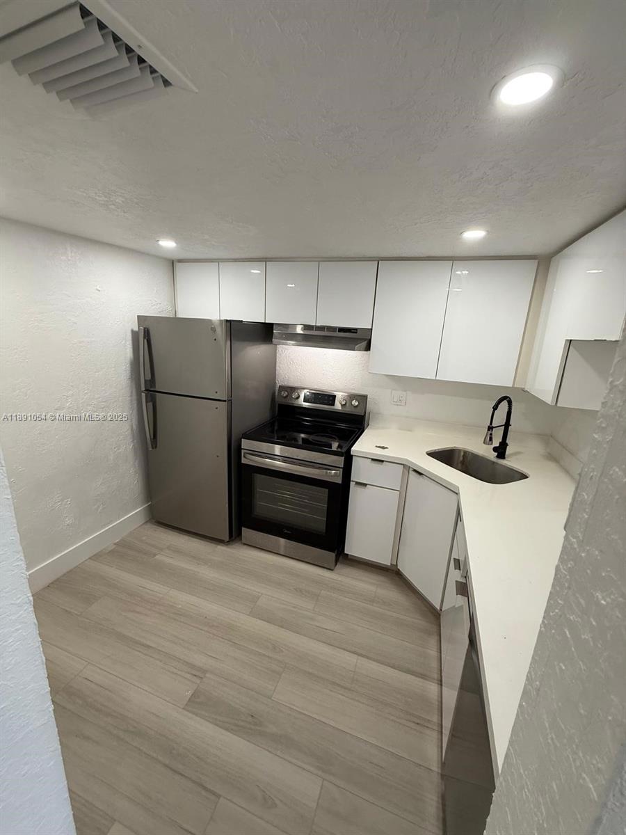 A small kitchen features white cabinets, stainless steel appliances, and light wood-look flooring — 2655 NW 60th Way # 195, Sunrise FL 33313, SUNRISE, FL