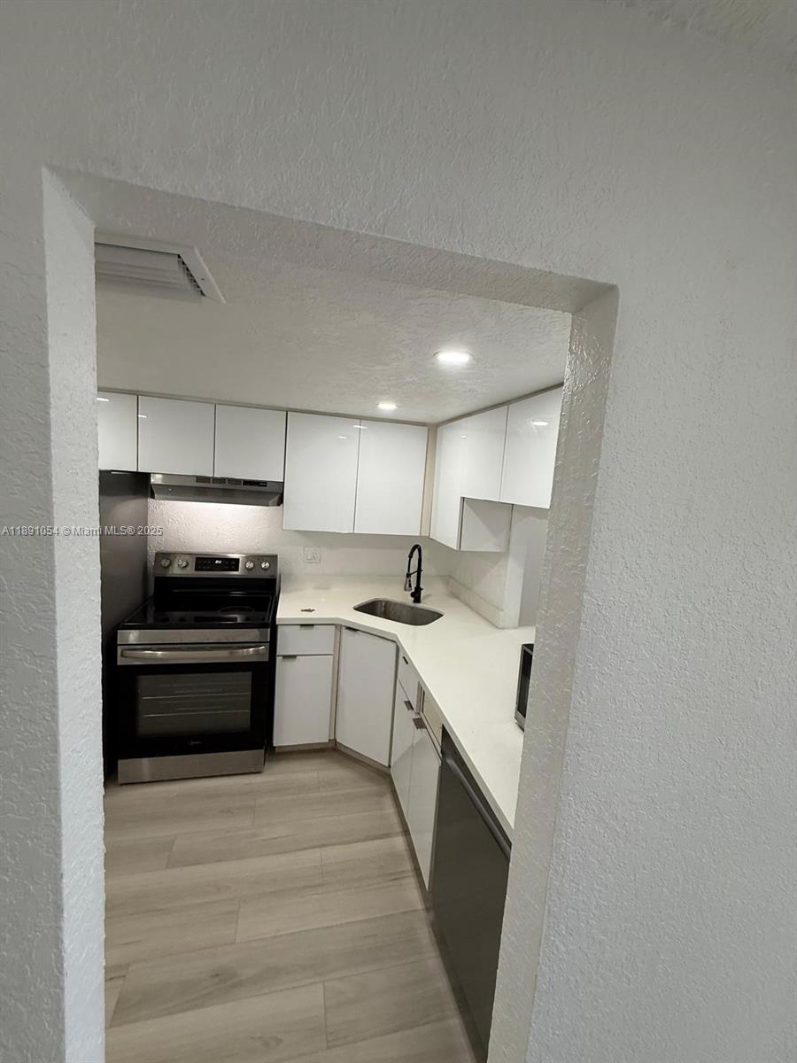 A galley-style kitchen features white cabinets, stainless steel appliances, and light-colored wood-look flooring — 2655 NW 60th Way # 195, Sunrise FL 33313, SUNRISE, FL