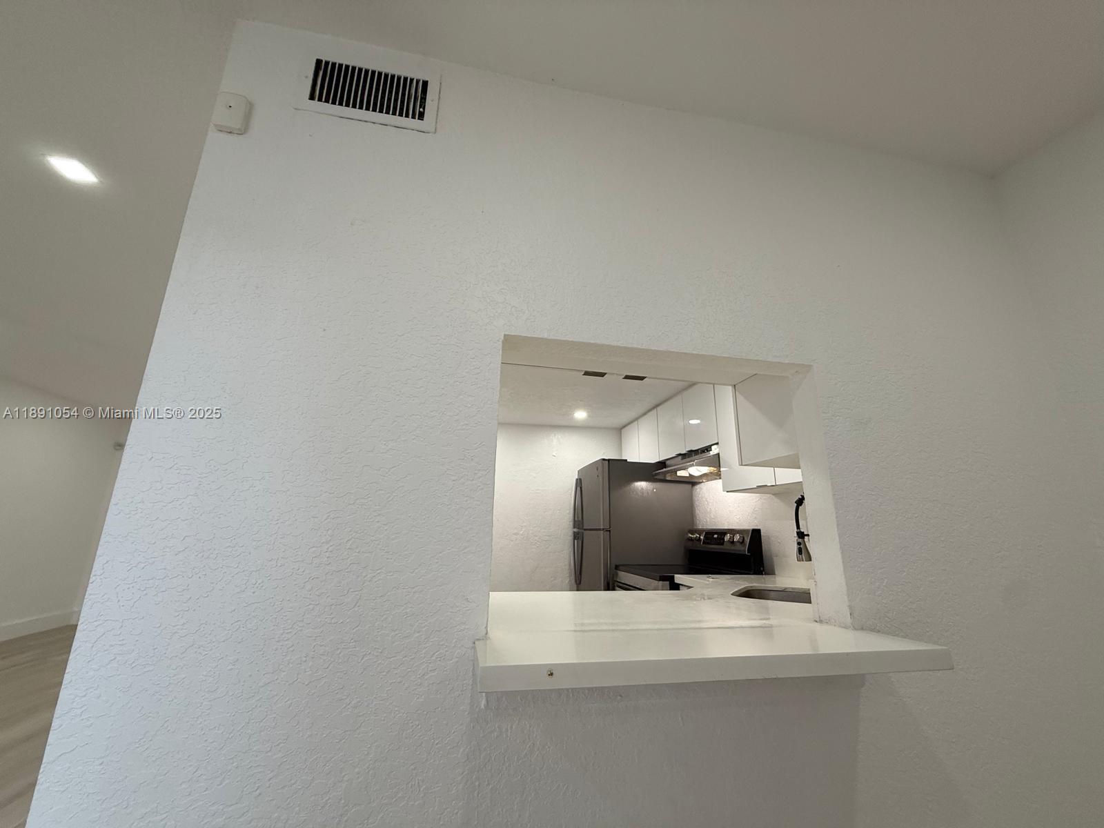 A kitchen pass-through window with a white counter looks into a kitchen with appliances — 2655 NW 60th Way # 195, Sunrise FL 33313, SUNRISE, FL