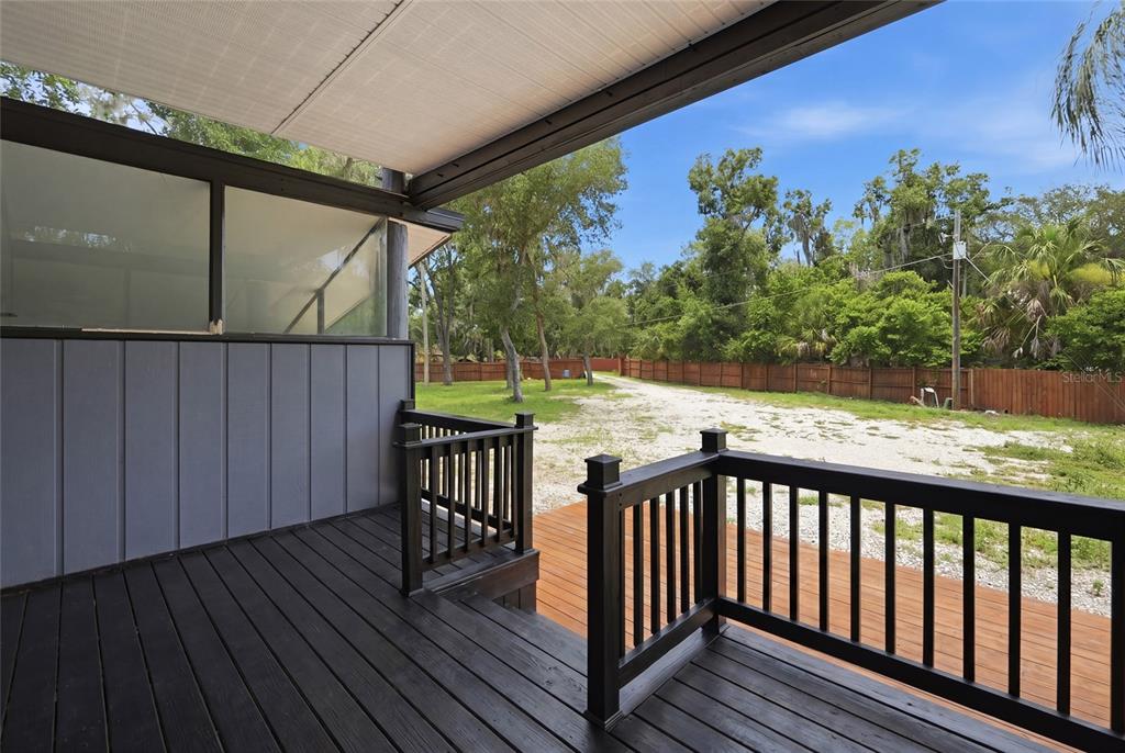 A dark wooden deck with railings overlooks a gravel yard and a wooden fence — 7210 VALRIE LANE, RIVERVIEW, FL