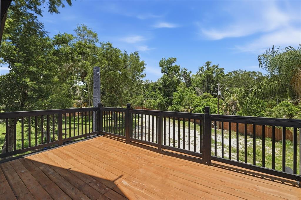 A wooden deck with black railings overlooks a grassy yard surrounded by mature trees — 7210 VALRIE LANE, RIVERVIEW, FL