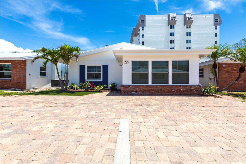 A white single-story house with blue shutters and a brick-based sunroom sits on a paver driveway — 6020 MIDNIGHT PASS ROAD UNIT 39, SARASOTA, FL