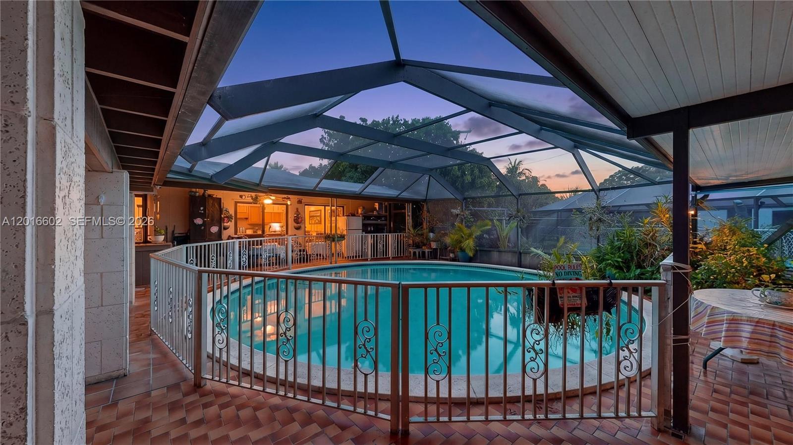 A screened-in patio features a curved swimming pool surrounded by a decorative metal fence — 10900 SW 177th Ter, Miami FL 33157, MIAMI, FL