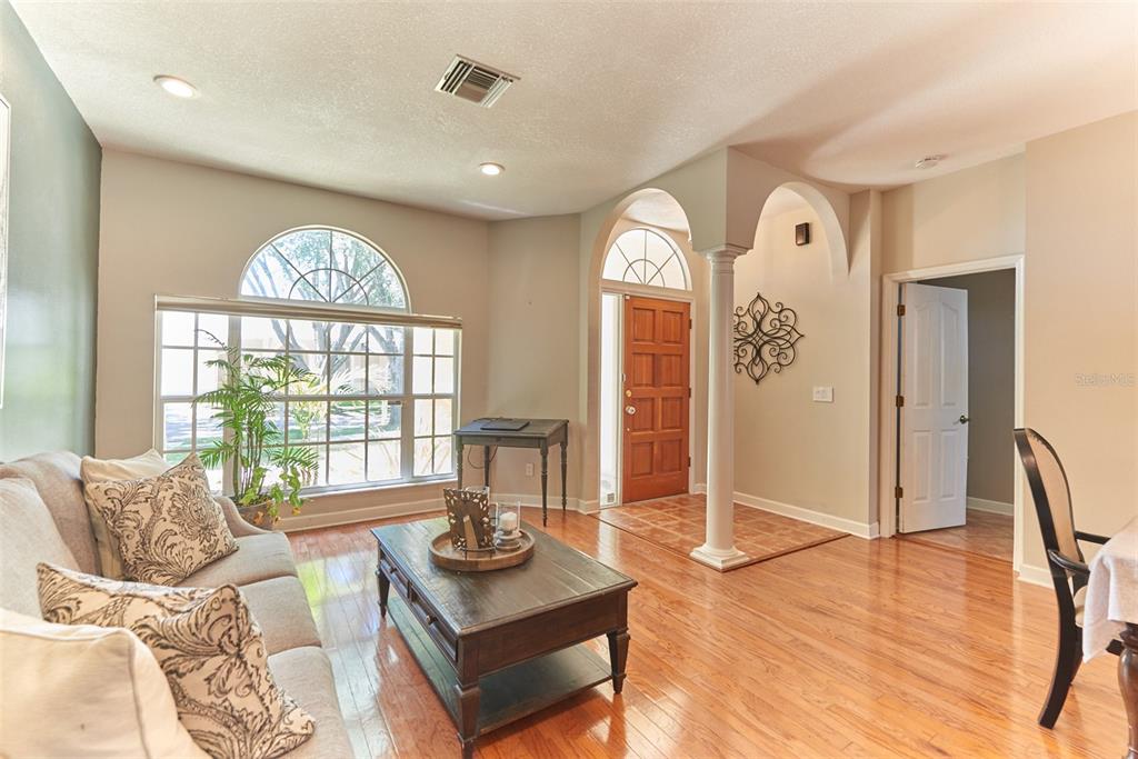 A living room with hardwood floors, a large arched window, and an arched entryway — 9302 HERITAGE OAK COURT, TAMPA, FL