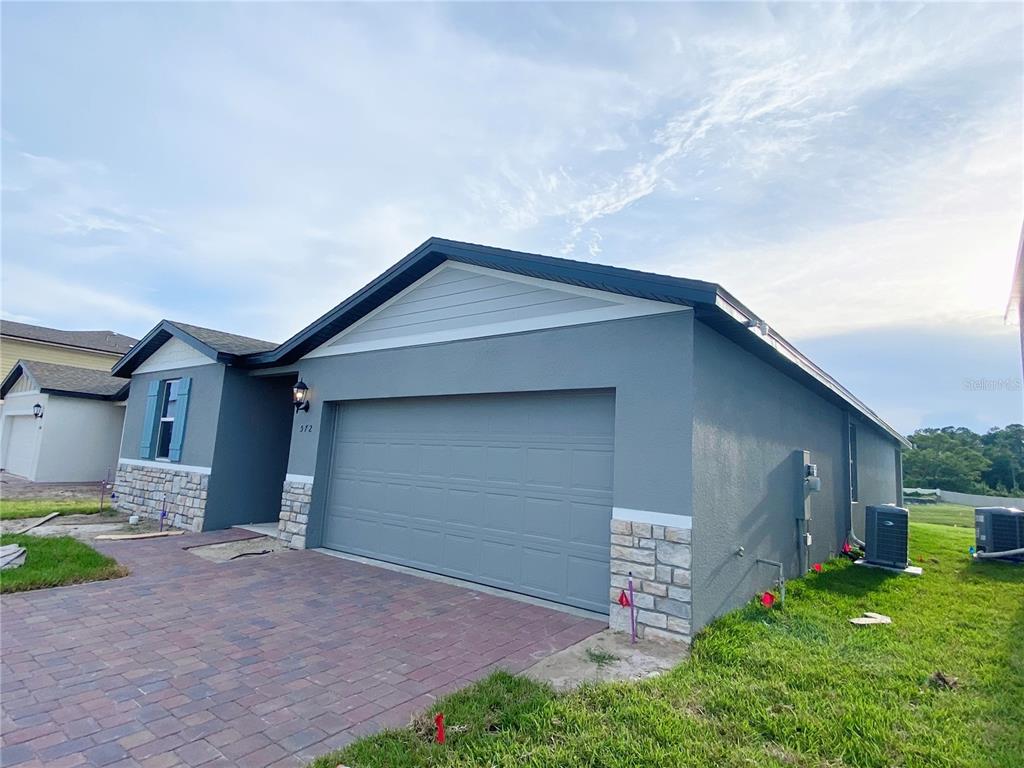 A gray single-story house with a stone veneer base and a brick paver driveway — 572 SUN WARBLER WAY, ST CLOUD, FL