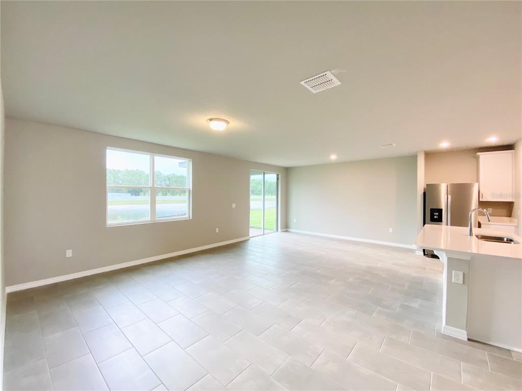 An open-concept living area features light gray tile flooring, neutral walls, and an adjacent kitchen — 572 SUN WARBLER WAY, ST CLOUD, FL