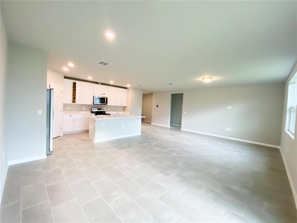 An open-concept kitchen and living area features white cabinetry, a central island, and tile flooring — 572 SUN WARBLER WAY, ST CLOUD, FL