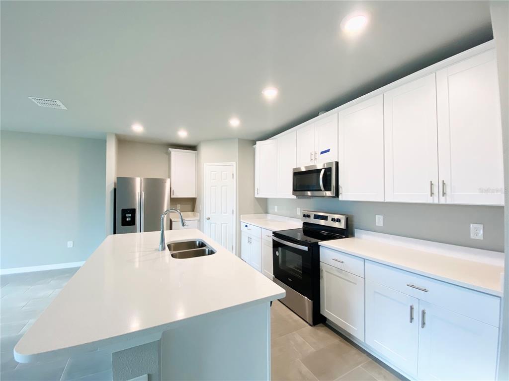 A modern kitchen features white cabinetry, stainless steel appliances, and a large central island — 572 SUN WARBLER WAY, ST CLOUD, FL