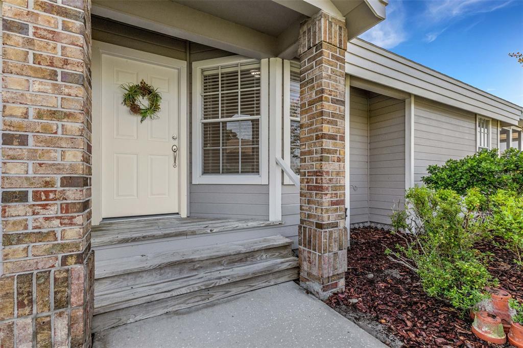 A front porch with wooden steps, a white door, and brick columns on a house — 1154 WATERFALL LANE UNIT n/a, LAKELAND, FL