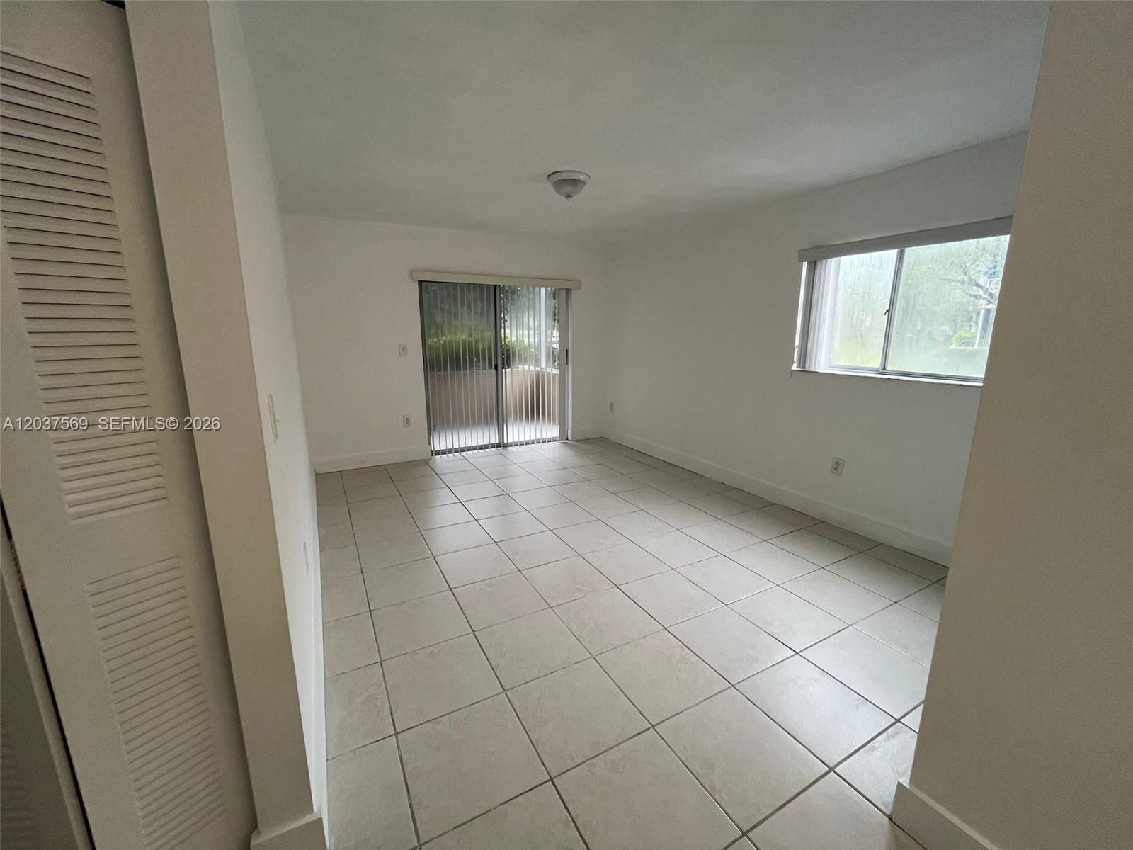 An empty room features white walls, light-colored tile flooring, a sliding glass door, and a window — 4800 NW 102nd Ave # 10, Doral FL 33178, DORAL, FL