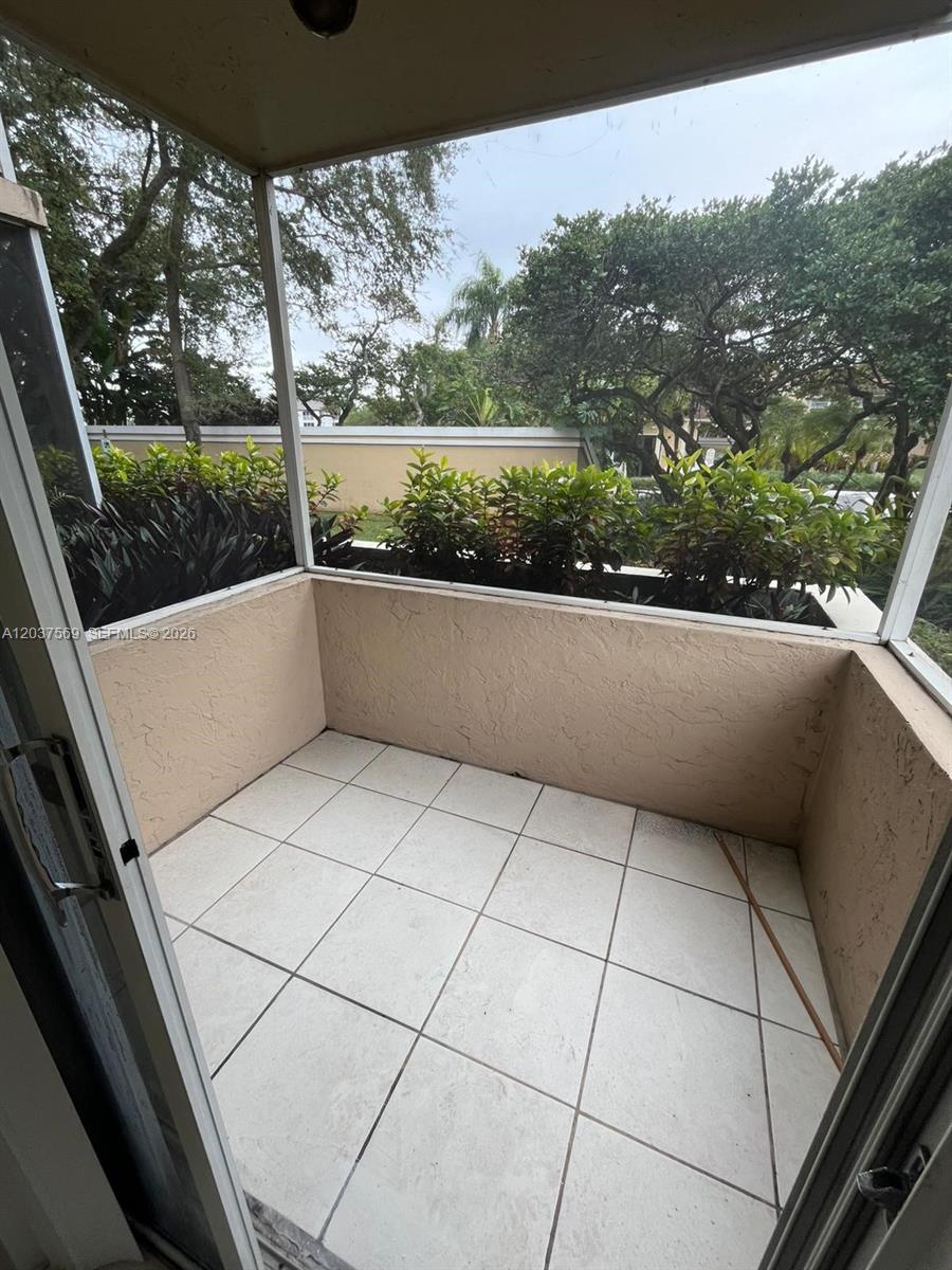 A screened-in balcony features light-colored floor tiles and a view of surrounding trees — 4800 NW 102nd Ave # 10, Doral FL 33178, DORAL, FL