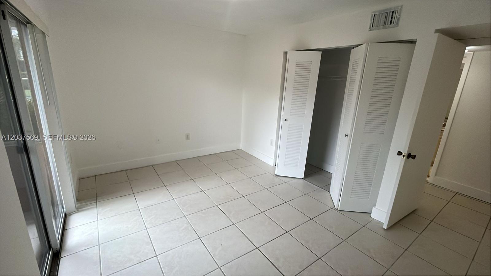 A bedroom with white walls, light-colored tile flooring, and a white louvered closet door — 4800 NW 102nd Ave # 10, Doral FL 33178, DORAL, FL