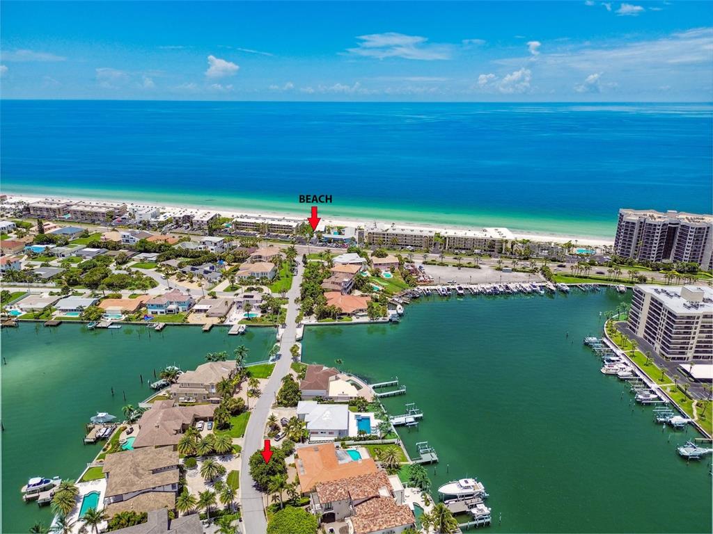 An aerial view shows a coastal neighborhood with waterfront homes, boat docks, and a beach — 205 HARRISON AVENUE, BELLEAIR BEACH, FL