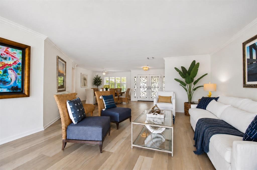A bright living room features white walls, light wood floors, a sofa, and accent chairs — 205 HARRISON AVENUE, BELLEAIR BEACH, FL