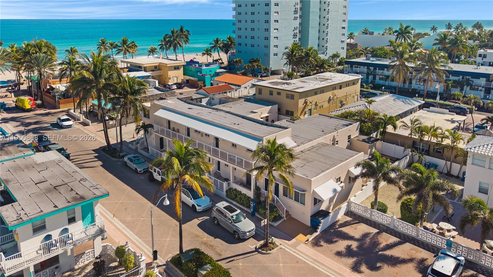 An aerial view shows a multi-story apartment building with palm trees near a beach — 320 New York St, Hollywood FL 33019, HOLLYWOOD, FL