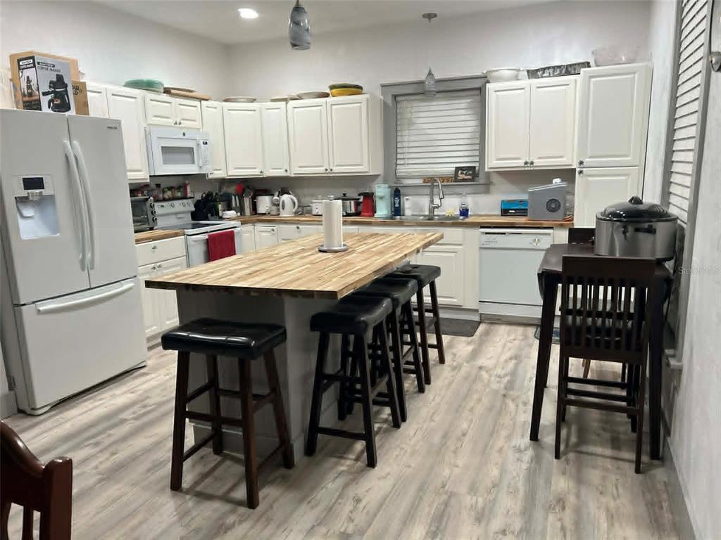A kitchen features white cabinets, a wood-topped island with stools, and light wood-look flooring — 2028 OLD NEW YORK AVENUE, DELAND, FL