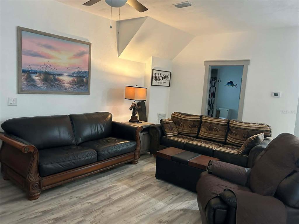A living room features a dark leather sofa, a patterned sofa, and light wood-look flooring — 2028 OLD NEW YORK AVENUE, DELAND, FL