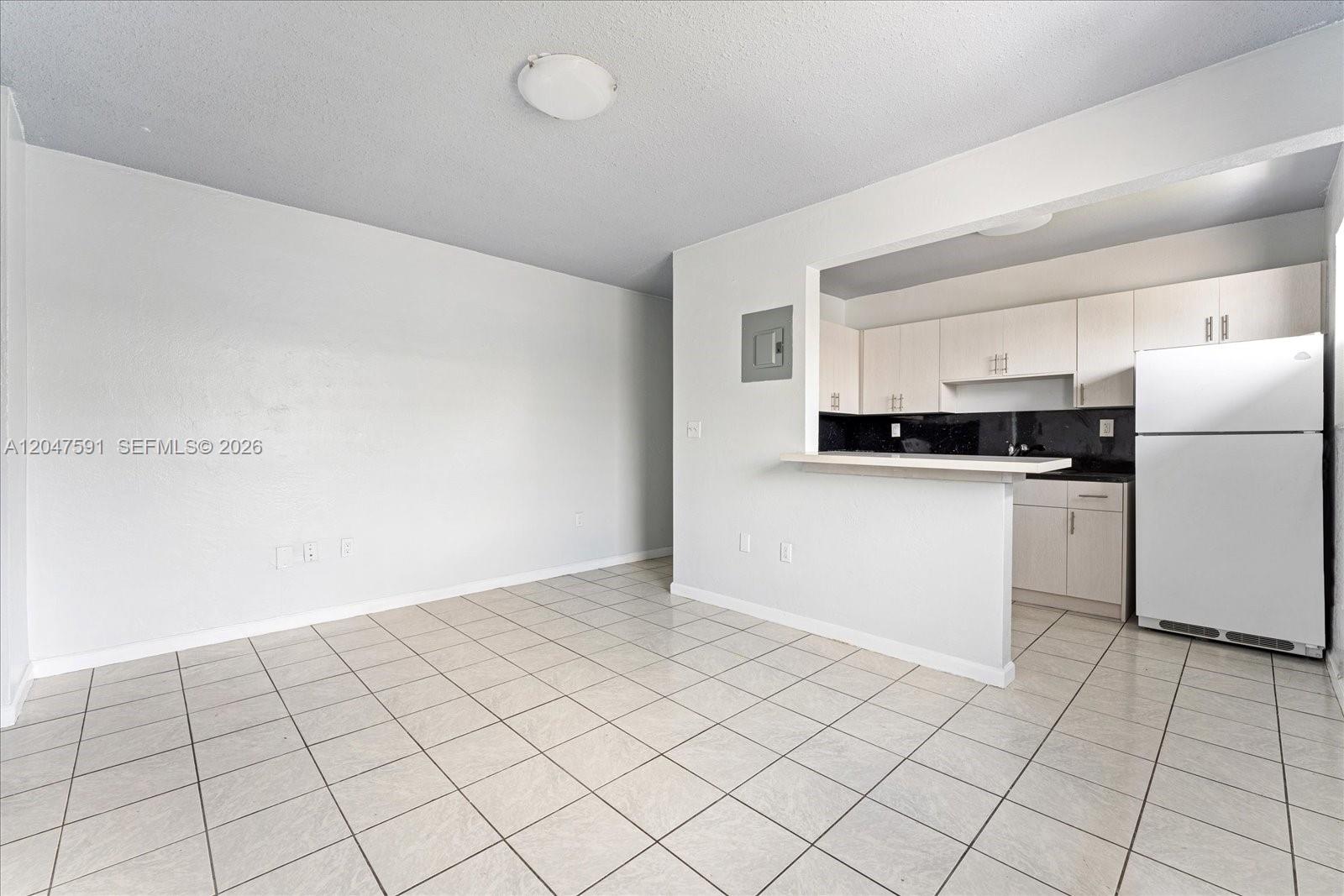A dining area with tiled floors opens to a kitchen featuring white cabinets and appliances — 3255 W Flagler St # 2, Miami FL 33135, MIAMI, FL