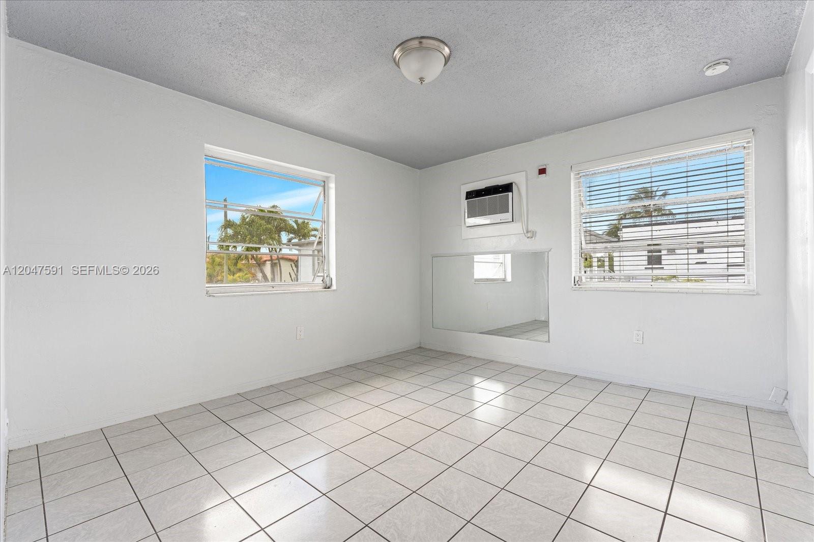 An empty room features white walls, tiled floors, two windows, and a wall-mounted air conditioner — 3255 W Flagler St # 2, Miami FL 33135, MIAMI, FL