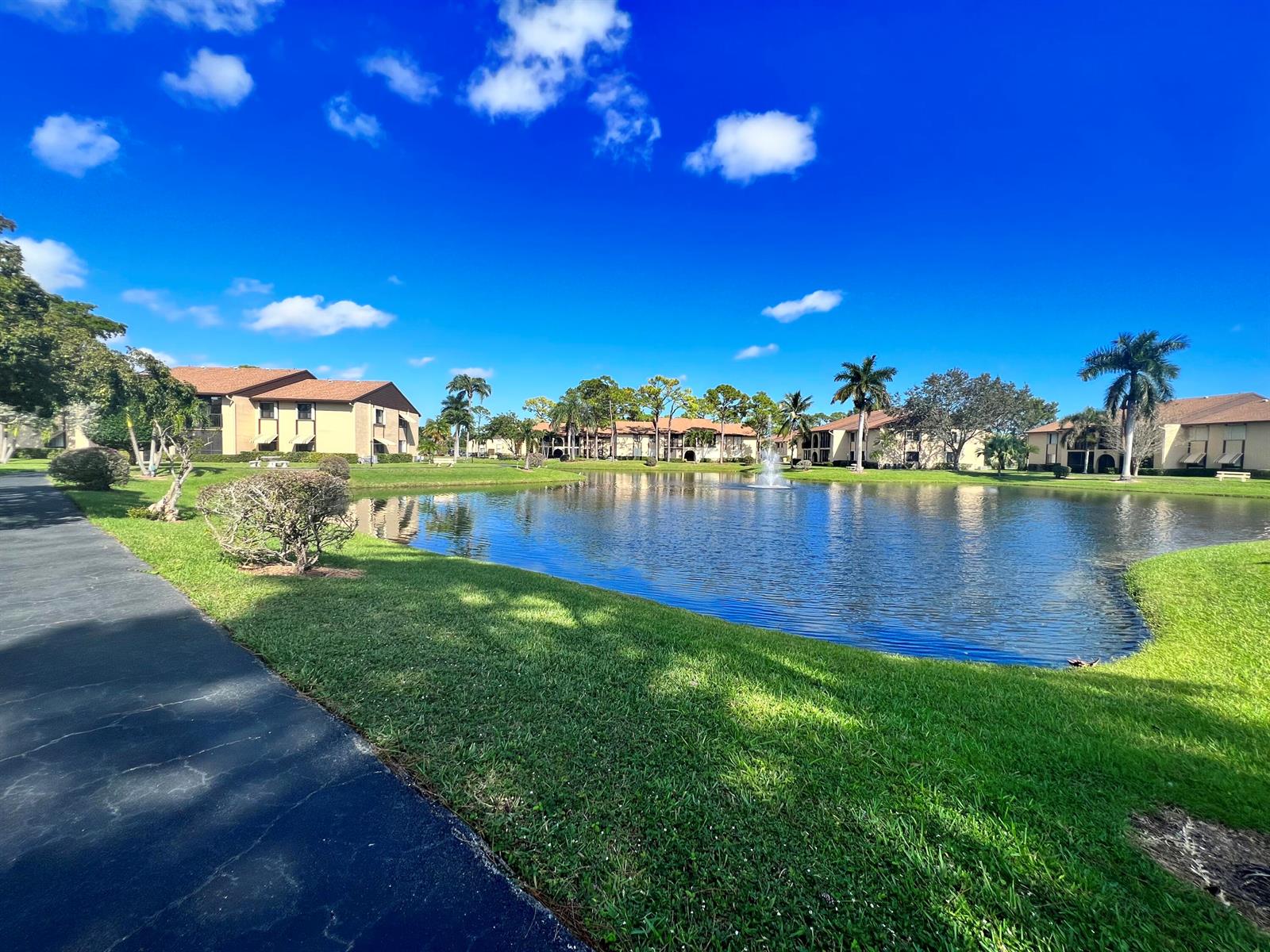 A pond with a fountain sits in front of apartment buildings surrounded by palm trees — 231 Pine Hov Circle # 1, FL 33463, FL