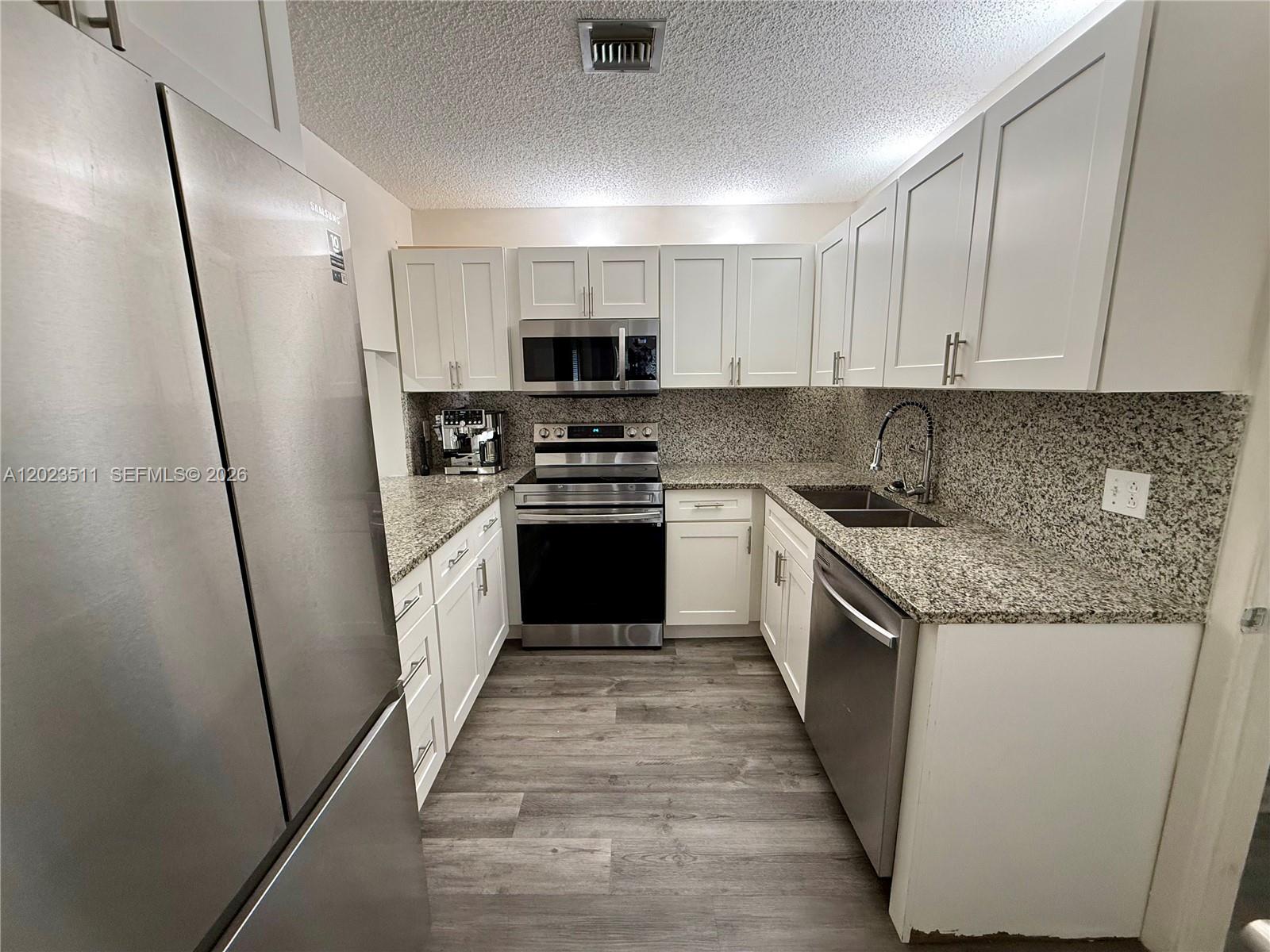 A galley kitchen features white cabinets, granite countertops, stainless steel appliances, and wood-look flooring — 4300 S Landar Dr, Lake Worth FL 33463, LAKE WORTH, FL