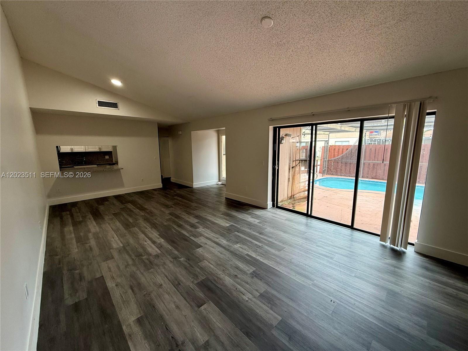 A living room with wood-look flooring features a kitchen pass-through and sliding glass doors — 4300 S Landar Dr, Lake Worth FL 33463, LAKE WORTH, FL