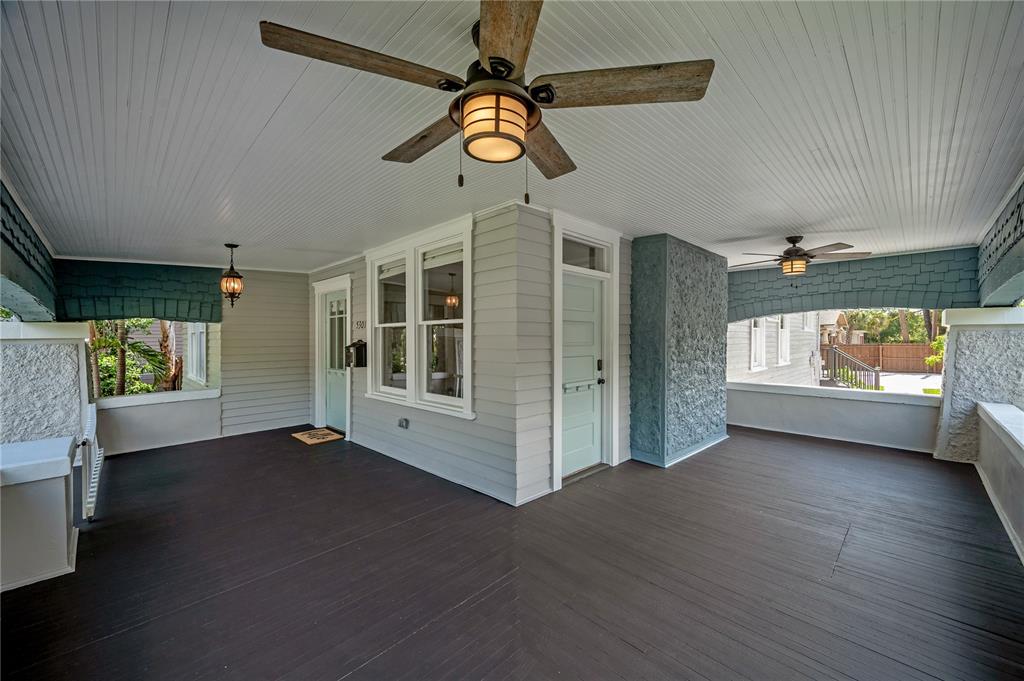 A spacious covered porch features dark wood flooring, two ceiling fans, and light-colored siding — 5301 N CENTRAL AVENUE, TAMPA, FL