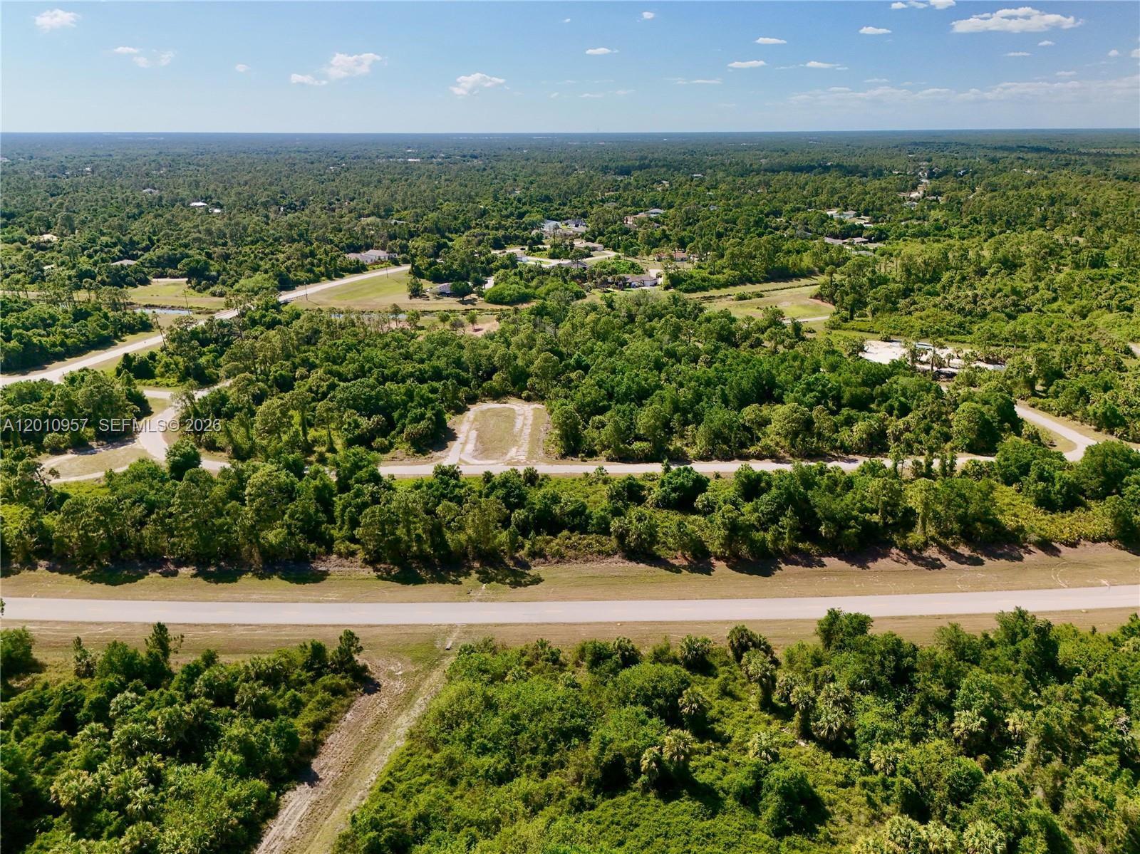 An aerial view shows a paved road running through a dense, wooded residential area — 0 CUSTER CIR, North Port FL 34288, NORTH PORT, FL