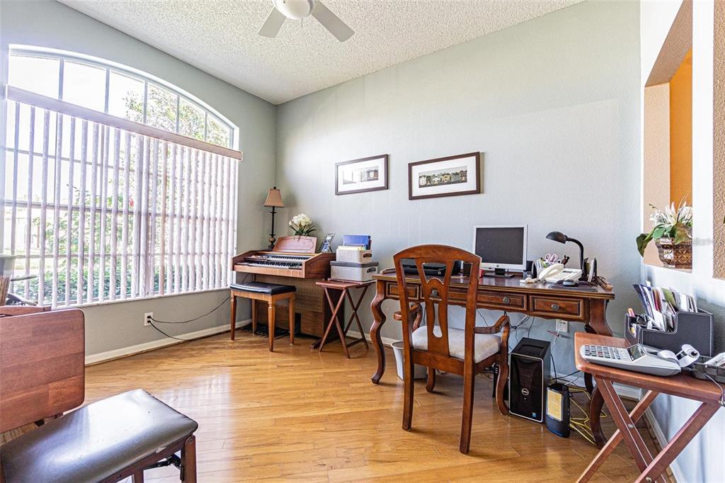 A home office features hardwood floors, a wooden desk, a piano, and a large window — 2514 SANDY HILL COURT, HOLIDAY, FL