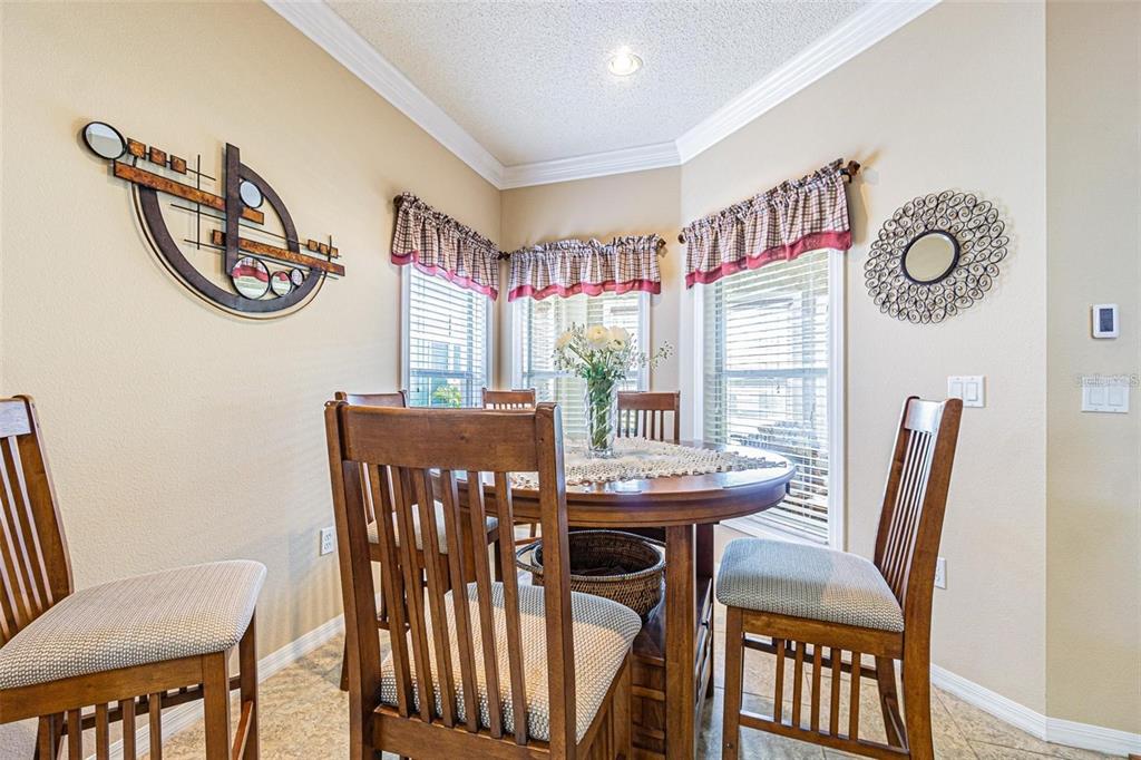A dining area features a round wooden table, four chairs, and windows with valances — 2514 SANDY HILL COURT, HOLIDAY, FL