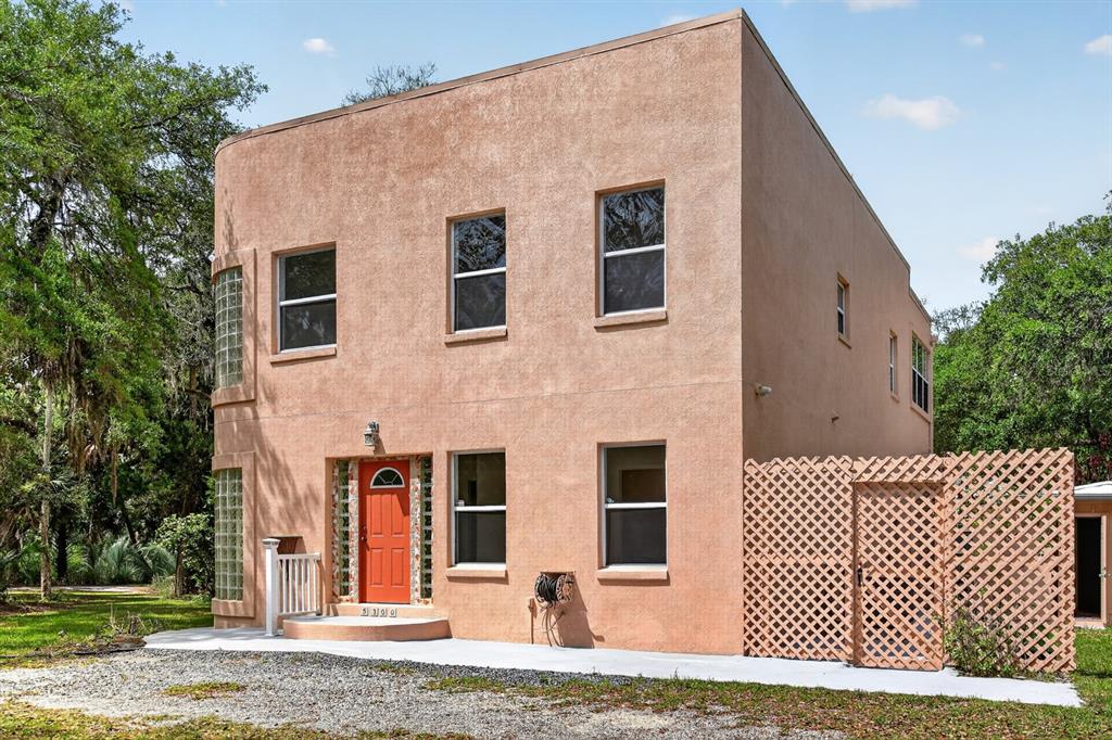 A two-story stucco house features a curved glass block corner, a red door, and lattice fencing — 5300 N OCEAN SHORE BOULEVARD, PALM COAST, FL