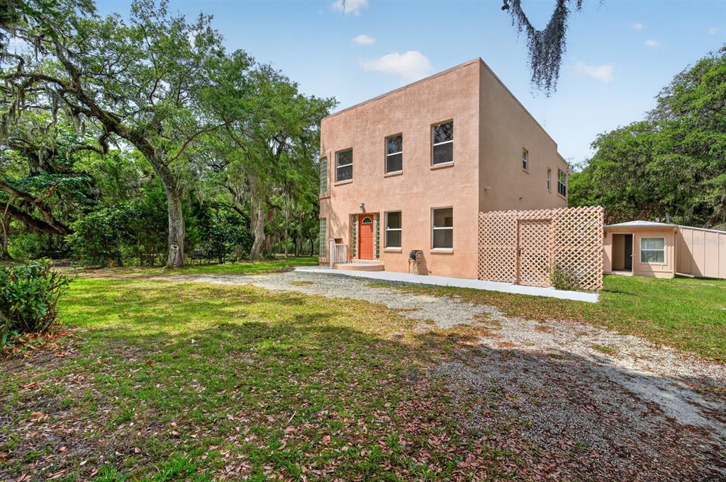 A two-story tan stucco house stands on a gravel driveway surrounded by large oak trees — 5300 N OCEAN SHORE BOULEVARD, PALM COAST, FL