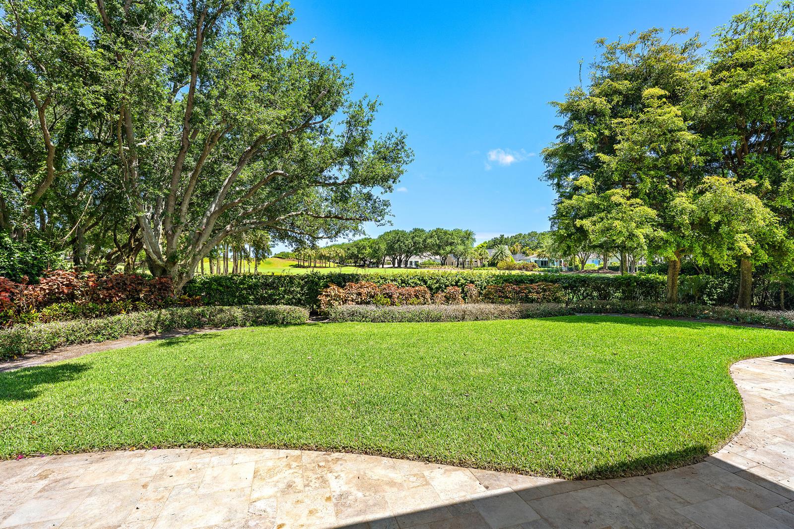 A stone patio overlooks a manicured lawn bordered by hedges and mature trees — 106 Commodore Drive, Jupiter FL 33477, JUPITER, FL