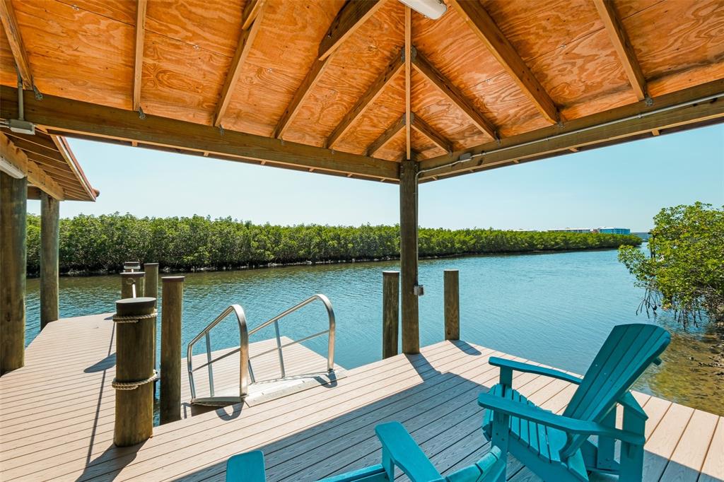 A covered wooden dock features teal Adirondack chairs and a metal ladder leading into water — 636 N RIVERSIDE DRIVE, NEW SMYRNA BEACH, FL