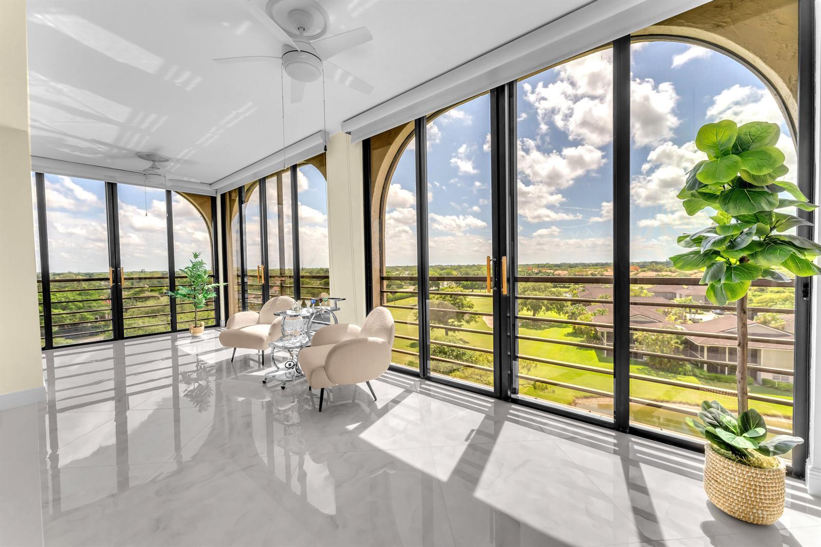 A sunroom with white tile floors, two armchairs, and floor-to-ceiling windows overlooking a golf course — 7578 Regency Lake Drive # 802, Boca Raton FL 33433, BOCA RATON, FL