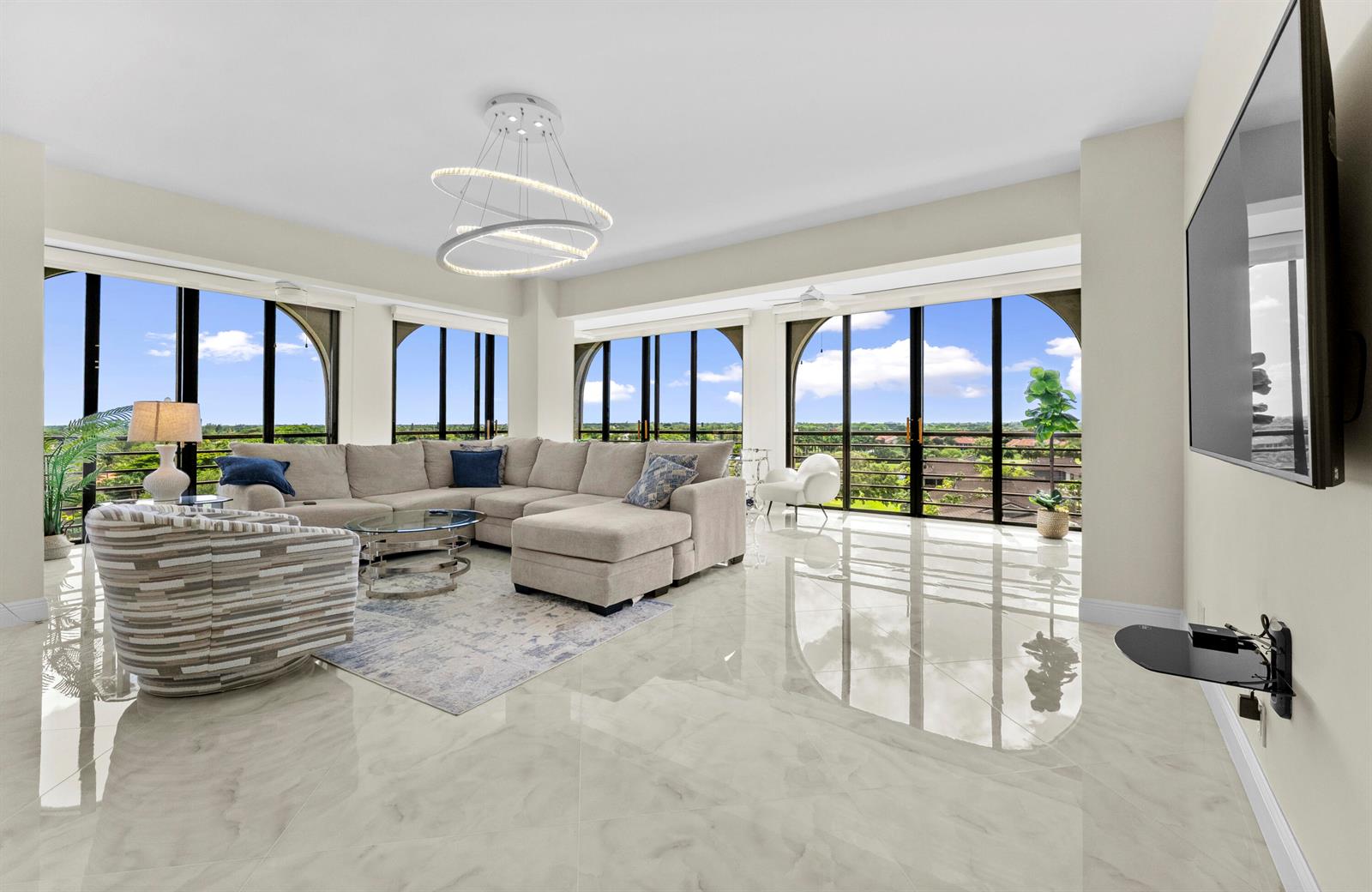 A bright living room features a large sectional sofa, marble-look tile floors, and floor-to-ceiling windows — 7578 Regency Lake Drive # 802, Boca Raton FL 33433, BOCA RATON, FL