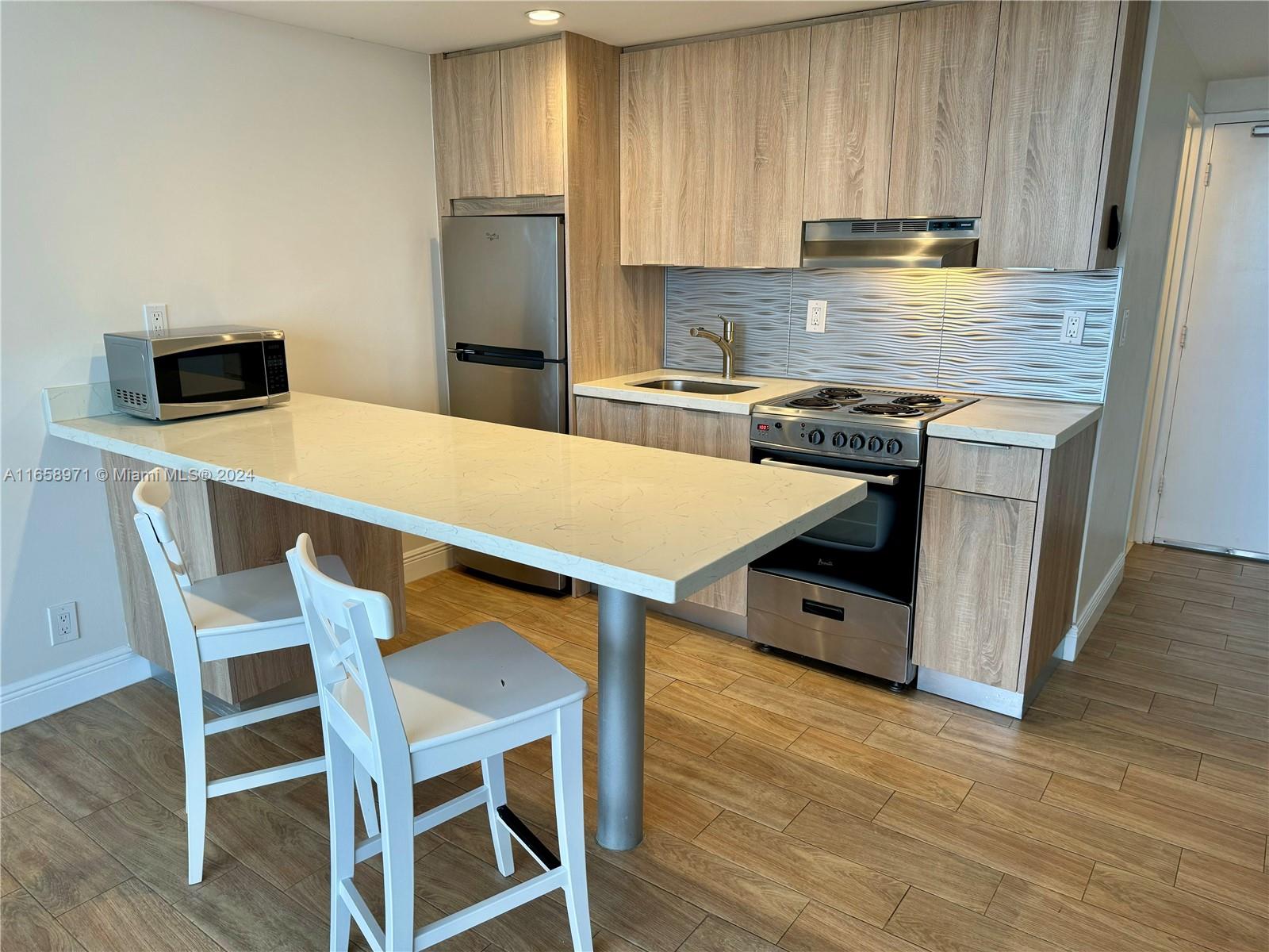 A kitchen features light wood cabinets, stainless steel appliances, a quartz breakfast bar, and stools — 1720 Harrison St # 15F, Hollywood FL 33020, HOLLYWOOD, FL