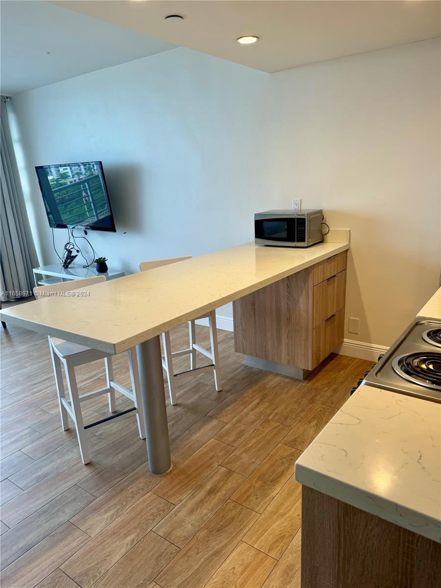 A kitchen features a long white quartz breakfast bar with wooden cabinets and two chairs — 1720 Harrison St # 15F, Hollywood FL 33020, HOLLYWOOD, FL