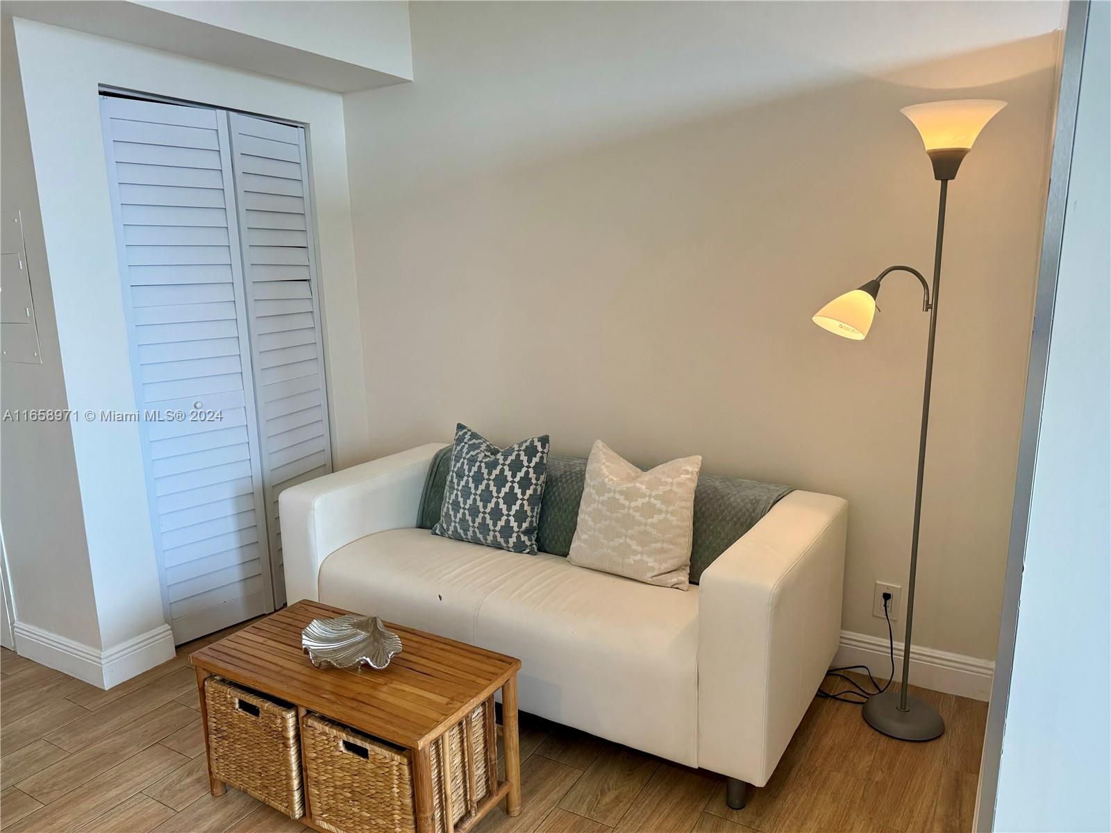 A white sofa, wooden coffee table with baskets, and floor lamp sit in a room — 1720 Harrison St # 15F, Hollywood FL 33020, HOLLYWOOD, FL