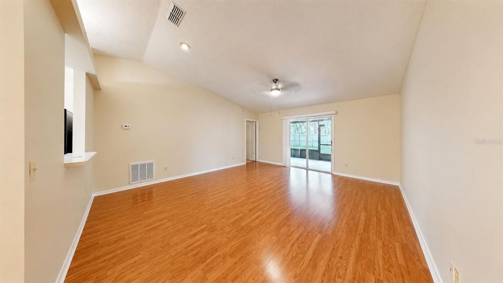 An empty living room features wood-look flooring, a vaulted ceiling, and sliding glass patio doors — 127 TITAN DRIVE, DAVENPORT, FL