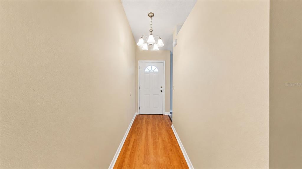 A hallway with light-colored walls, wood-look flooring, and a white door with a glass insert — 127 TITAN DRIVE, DAVENPORT, FL
