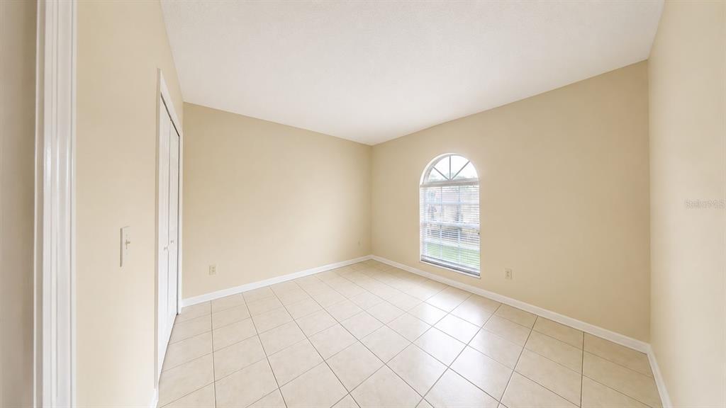 An empty bedroom features beige walls, white trim, tile flooring, and an arched window — 127 TITAN DRIVE, DAVENPORT, FL