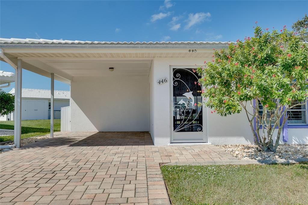 A white house exterior features a paved carport, a decorative screen door, and a small tree — 446 CIRCLEWOOD DRIVE UNIT L2, VENICE, FL