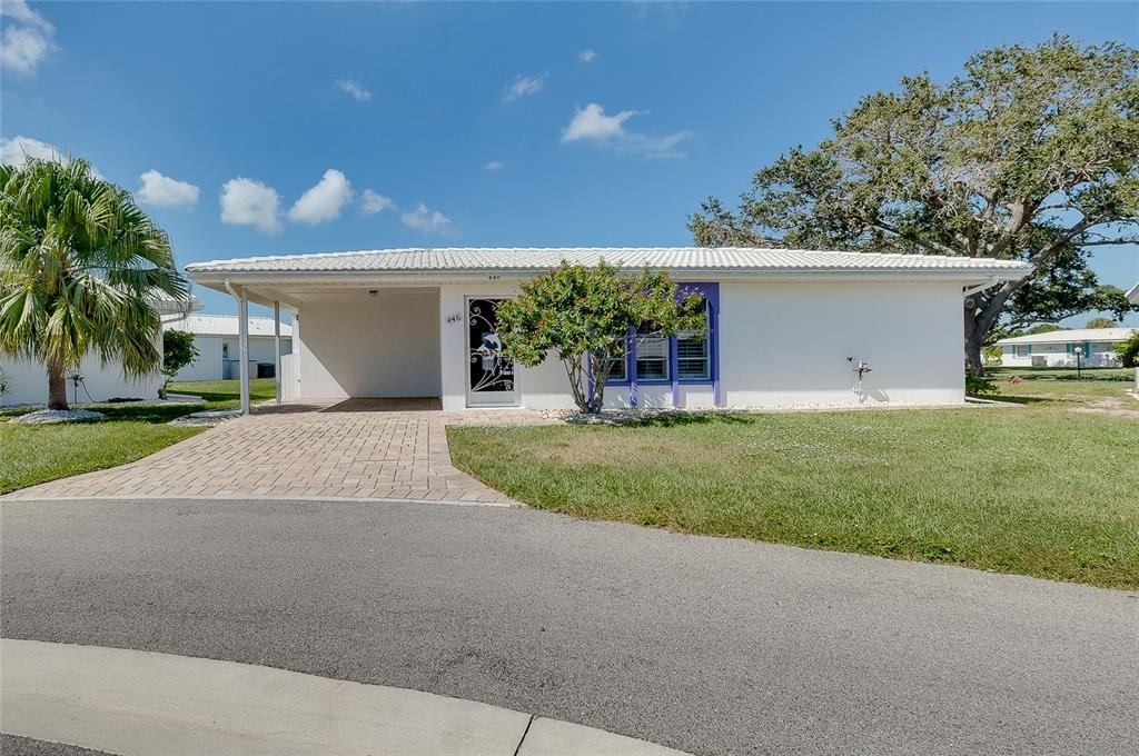 A white single-story house features a paved carport, a front door, and a large tree — 446 CIRCLEWOOD DRIVE UNIT L2, VENICE, FL