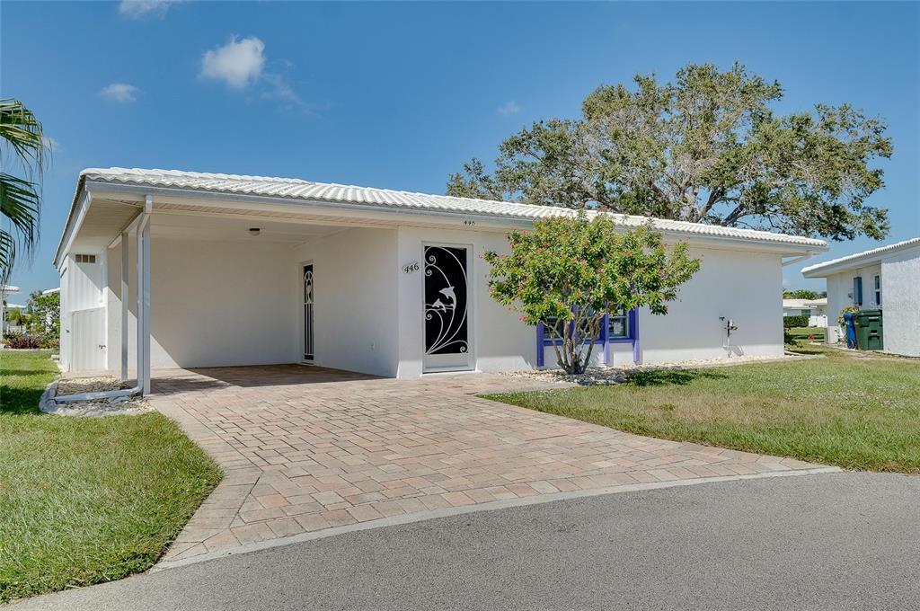 A white single-story house features a paved driveway, a carport, and a decorative front door — 446 CIRCLEWOOD DRIVE UNIT L2, VENICE, FL