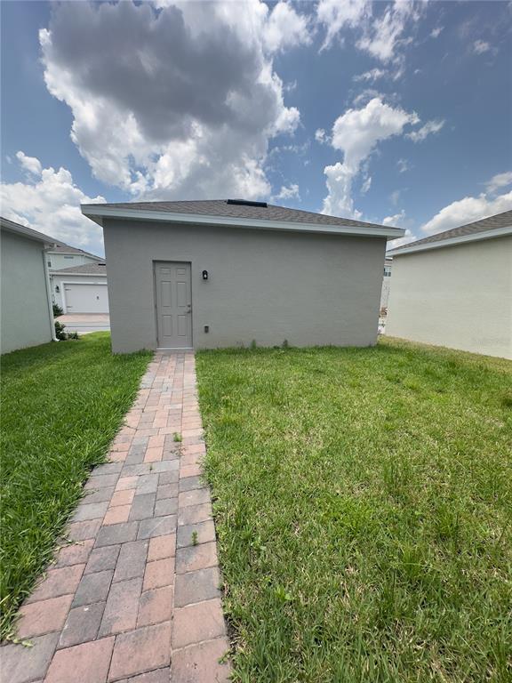 A gray exterior wall with a single door and a brick walkway in a yard — 12560 WESTHAVEN OAK DRIVE, WINTER GARDEN, FL