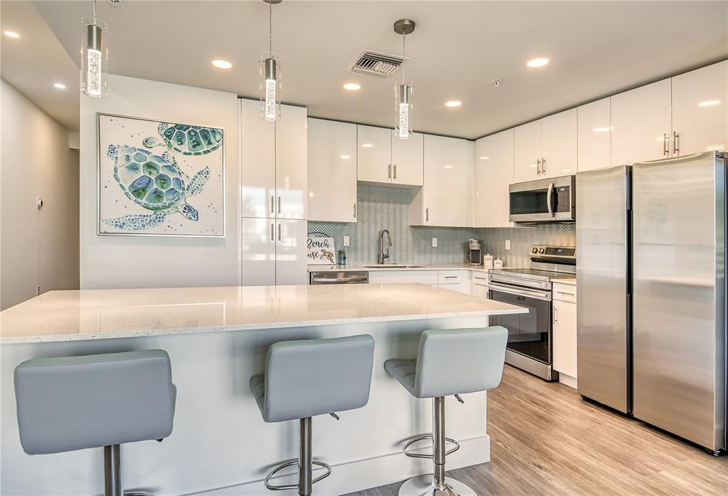 A modern kitchen features white cabinets, stainless steel appliances, a quartz island, and three barstools — 1709 N TAMIAMI TRAIL UNIT 221, SARASOTA, FL