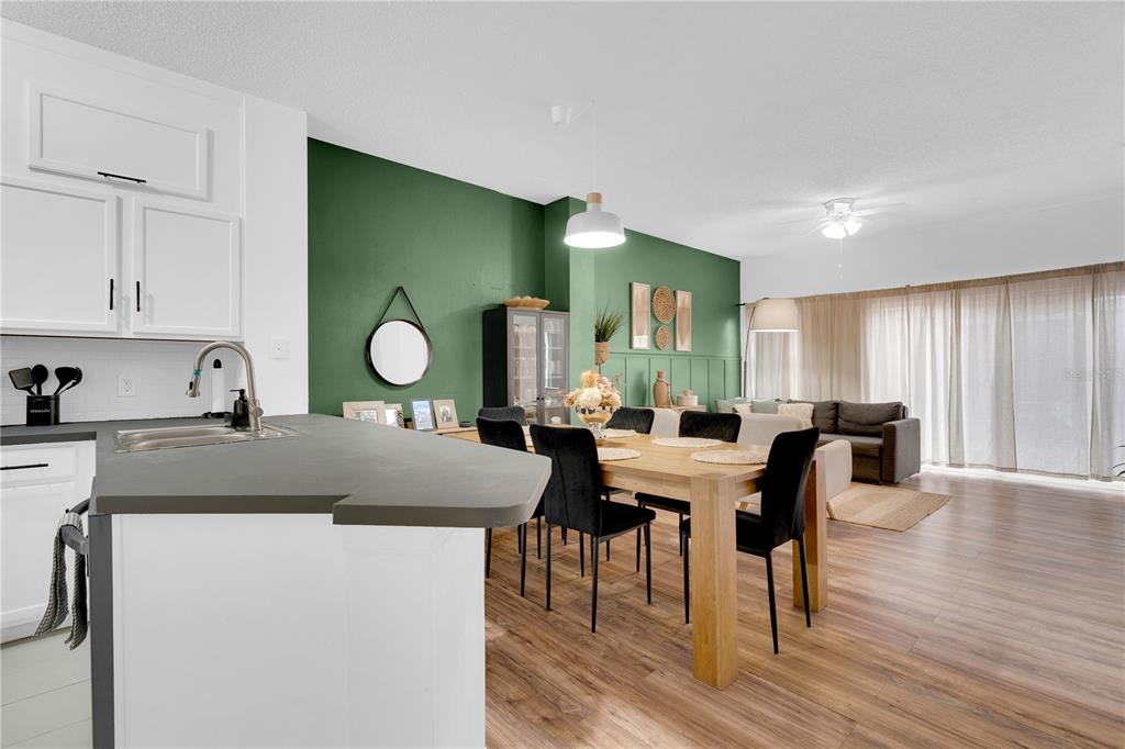 A kitchen with a dark countertop overlooks a dining area and living room with green walls — 4703 VERO BEACH PLACE, KISSIMMEE, FL