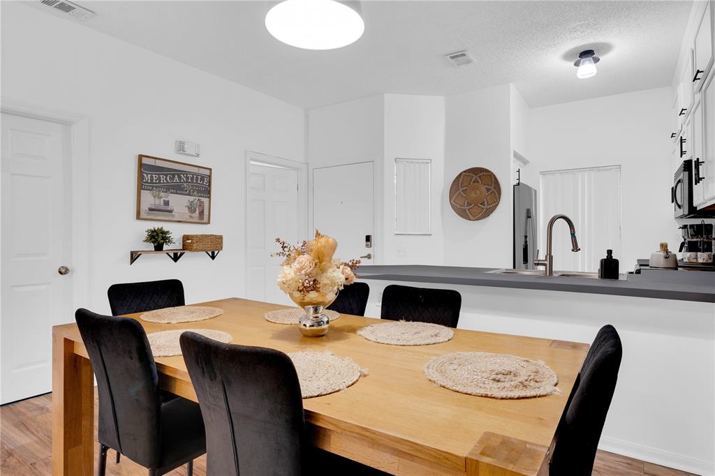 A dining area with a wooden table and black chairs sits adjacent to a kitchen — 4703 VERO BEACH PLACE, KISSIMMEE, FL